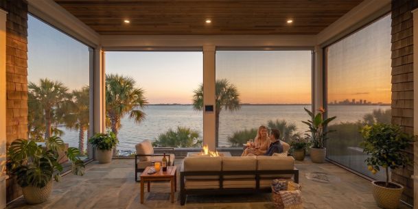 Couple relaxing on a screened waterfront patio with motorized shades at sunset